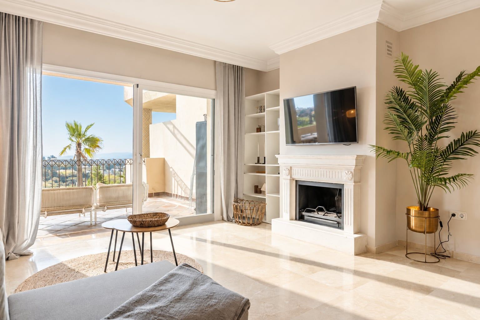A spacious living room with a television, a fireplace, a balcony with a view, and a potted plant.