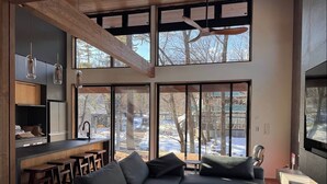 A modern living room with a large sectional sofa, a coffee table, and a kitchen area with bar stools. - Forest Gardens (Hakuba)