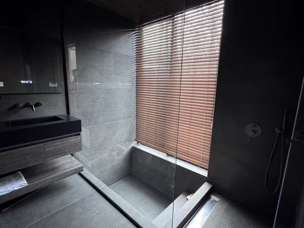 A modern bathroom with a dark wood vanity, a glass shower enclosure, and a window with blinds. - Forest Gardens (Hakuba)