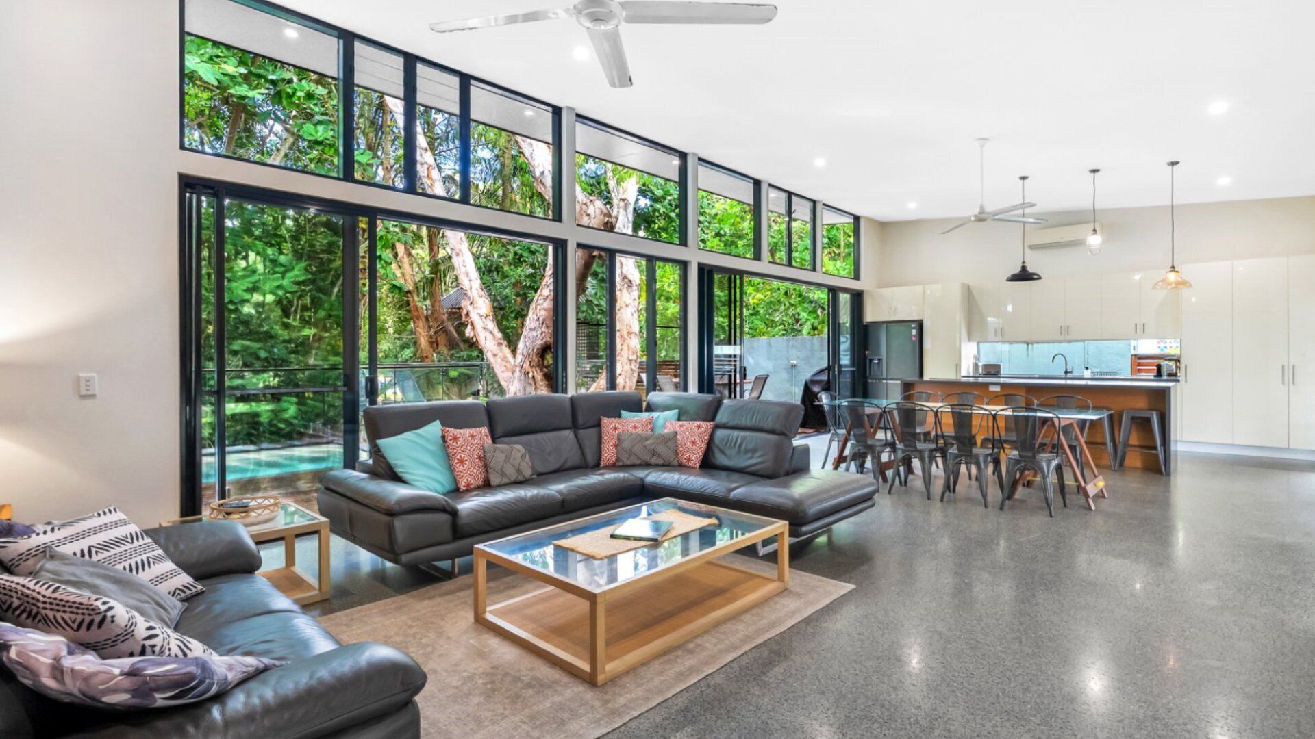 A modern living room with a sectional sofa, a glass coffee table, and a view of a lush garden through large windows.