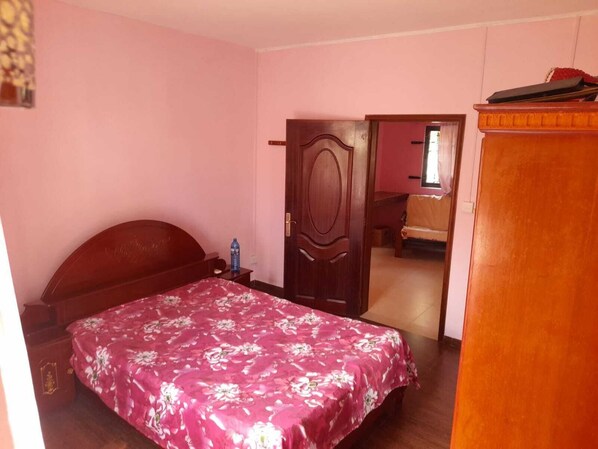 A bedroom with a wooden bed, a nightstand, a water bottle, and a wardrobe.