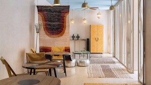 A modern interior with a dining area, a large abstract tapestry, and a view through a glass door. - Riad Romeo (Marrakech)