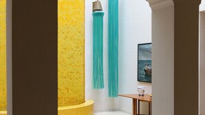 A room with a yellow tiled wall, a white column, and a wooden table with a chair. - Riad Romeo (Marrakech)