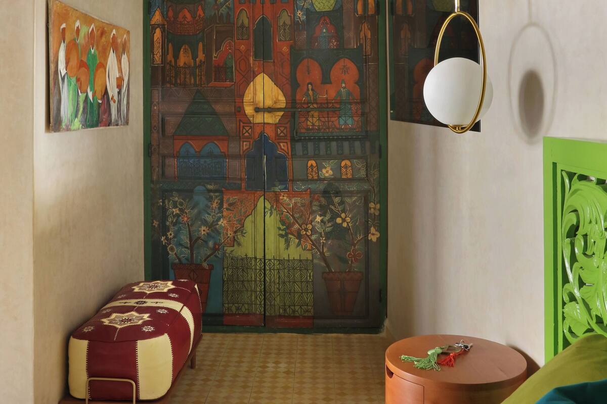 A room with a bed, a small table, a painting, and a decorative door.
