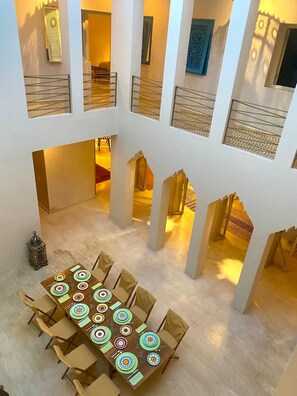 A spacious atrium with a high ceiling, multiple levels, and a central dining area with a long table set for a meal. - Riad Romeo (Marrakech)
