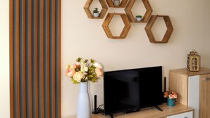 A modern living room with a flat-screen TV on a wooden TV stand, a decorative hexagonal wall art, and a striped panel on the left. - Colibri Castle View – Romantic Escape (Veliko Tarnovo)