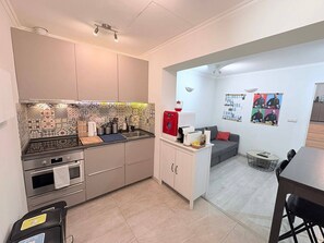 A compact kitchen with a tiled backsplash, a coffee machine, and a dining area with a sofa and table.