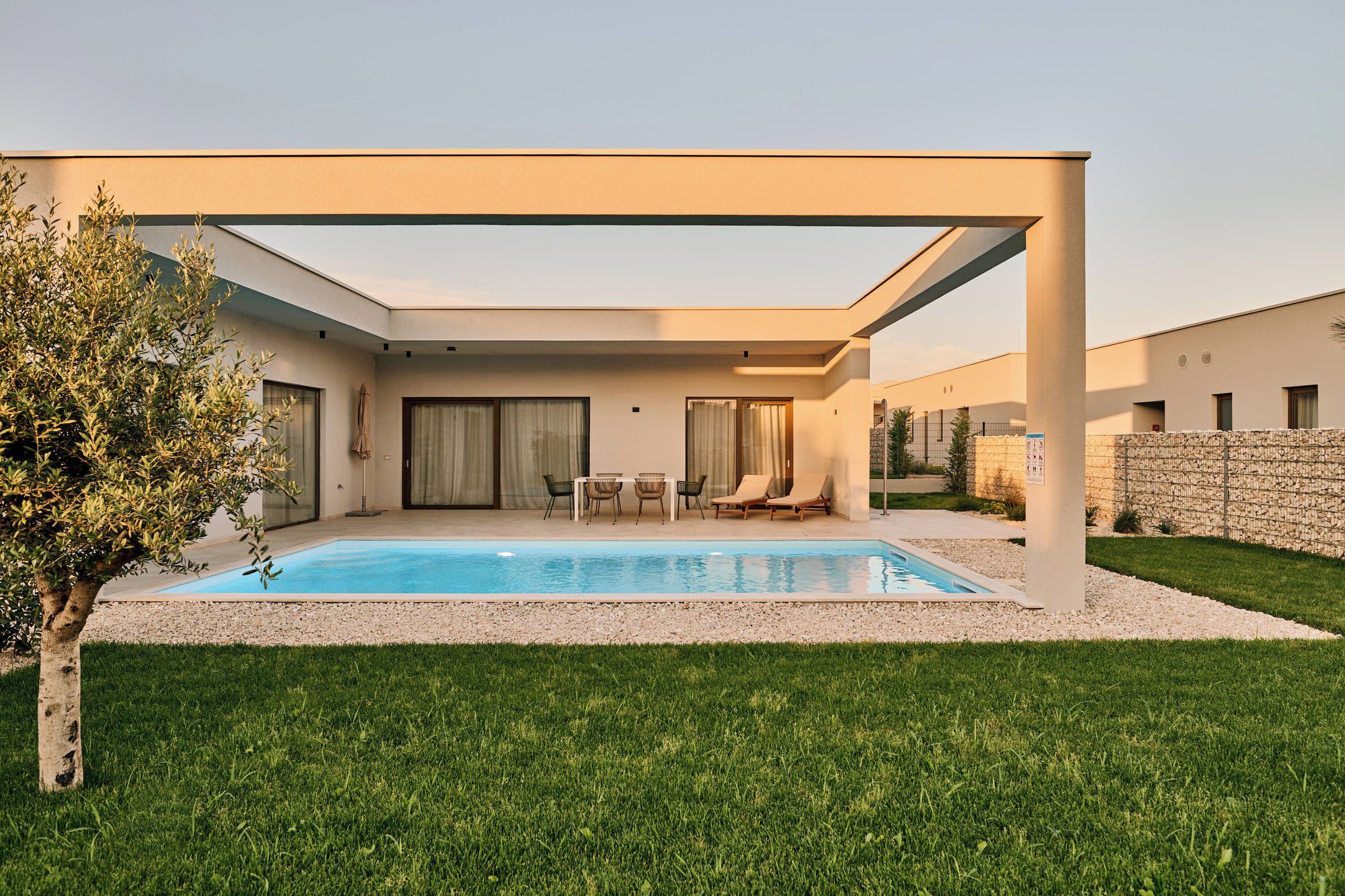 Une maison moderne dotée d’une piscine, d’un patio couvert et d’une pelouse bien entretenue.