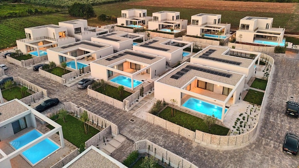 Un complexe résidentiel moderne comprenant plusieurs maisons, chacune dotée d’une piscine et de panneaux solaires sur le toit.