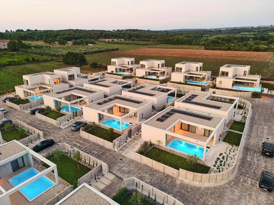 Un complejo residencial moderno con varias casas, cada una con piscina y paneles solares en el techo.