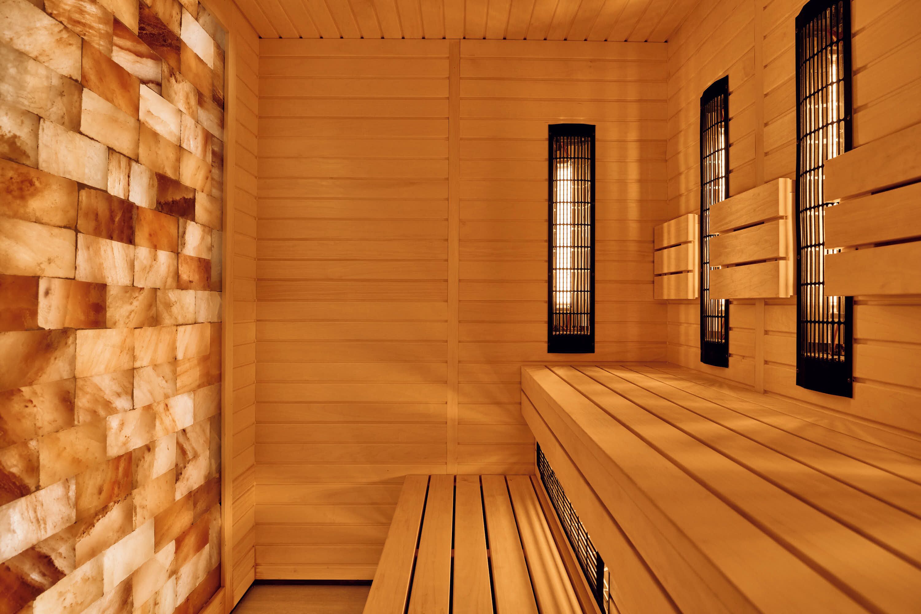 Un sauna aux murs et aux bancs en bois, avec un mur à motifs de briques sur le côté gauche et des fenêtres avec des grilles noires sur le côté droit.
