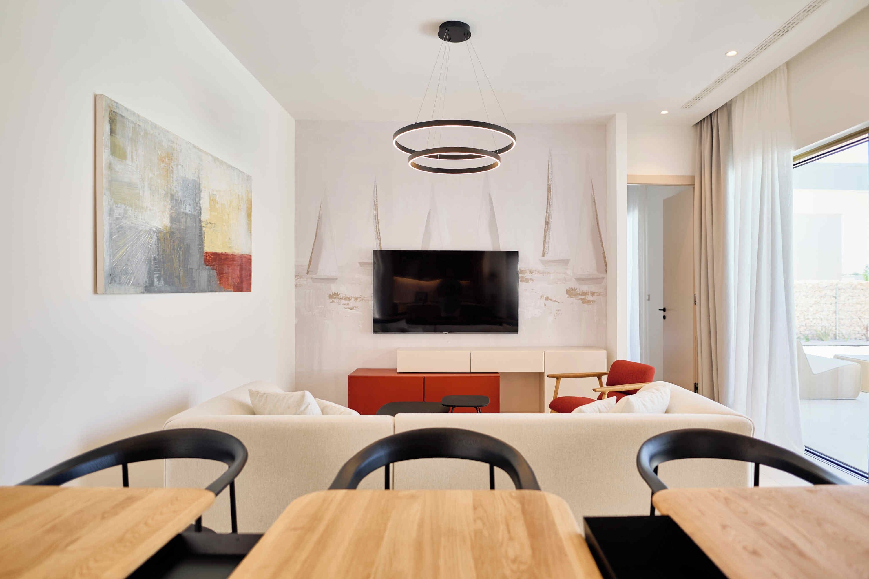 A modern living room with a large flat-screen TV, a wooden dining table, and a sofa.