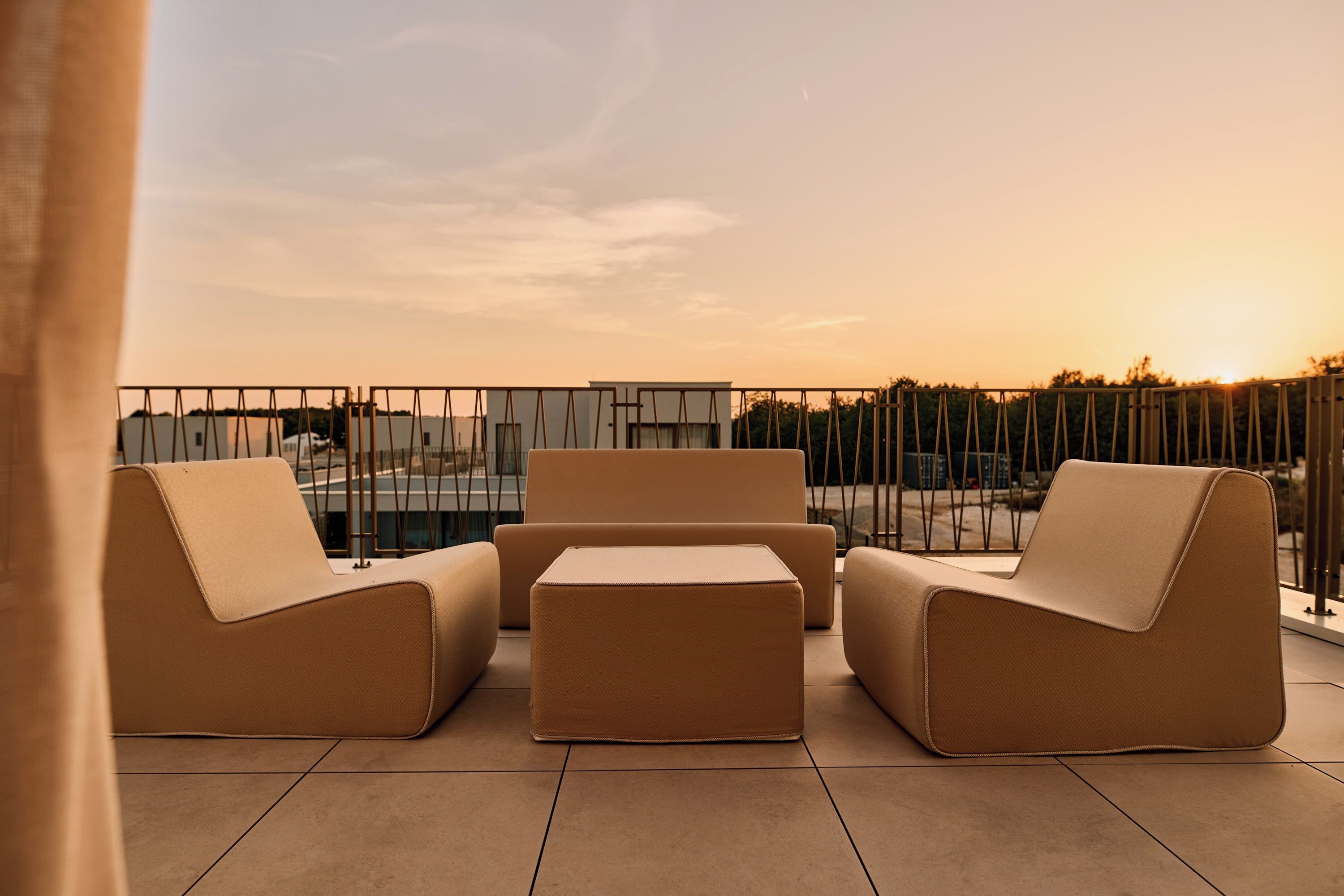 Une terrasse sur le toit, dotée de mobilier moderne, d’une rambarde et offrant une vue sur le coucher du soleil.