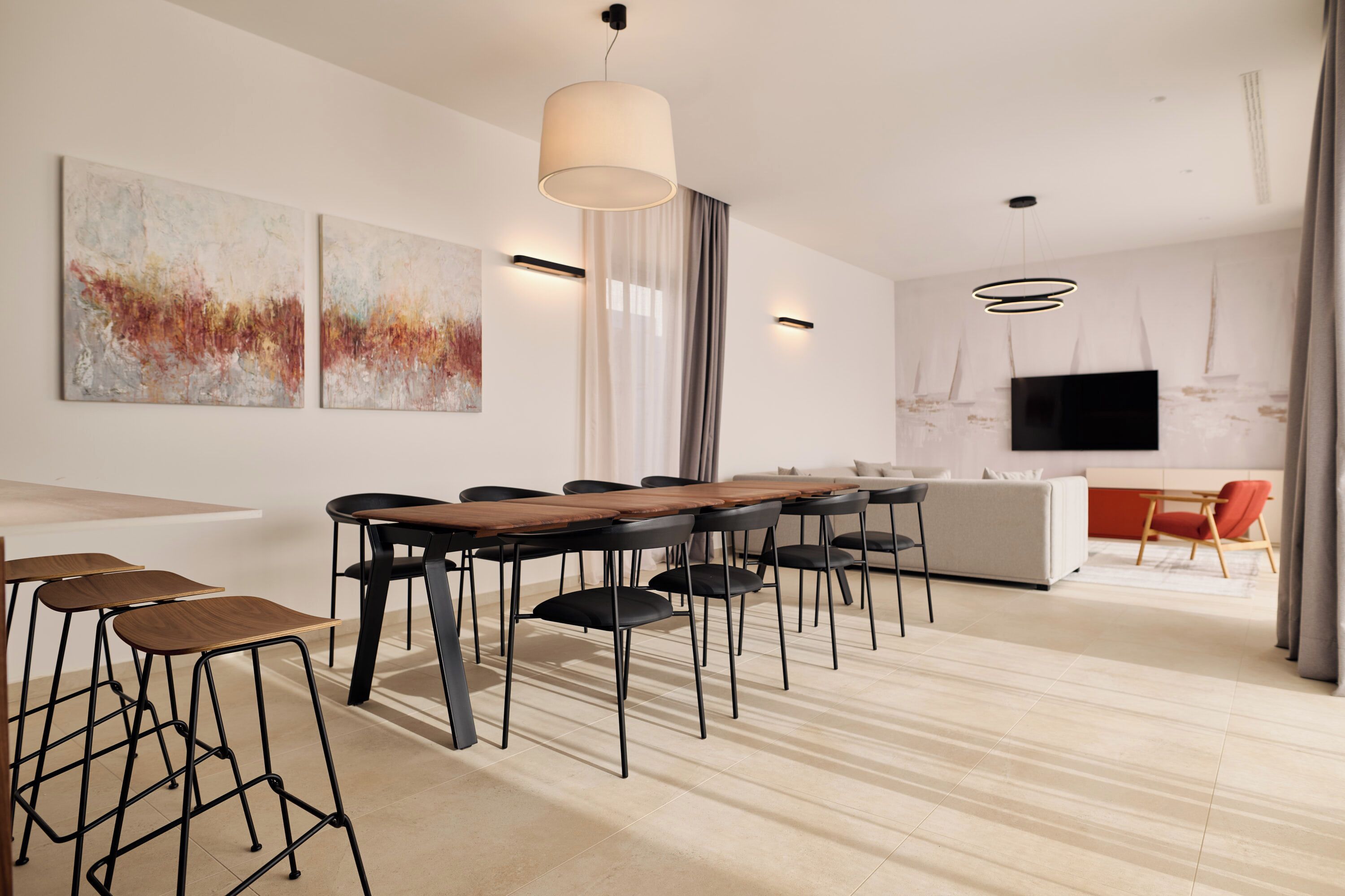 A modern dining area with a long wooden table, black chairs, and a bar stool area.