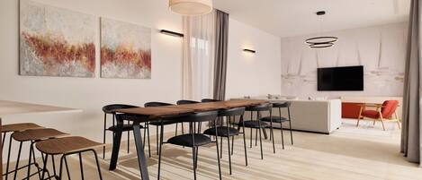 A modern dining area with a long wooden table, black chairs, and a bar stool area.