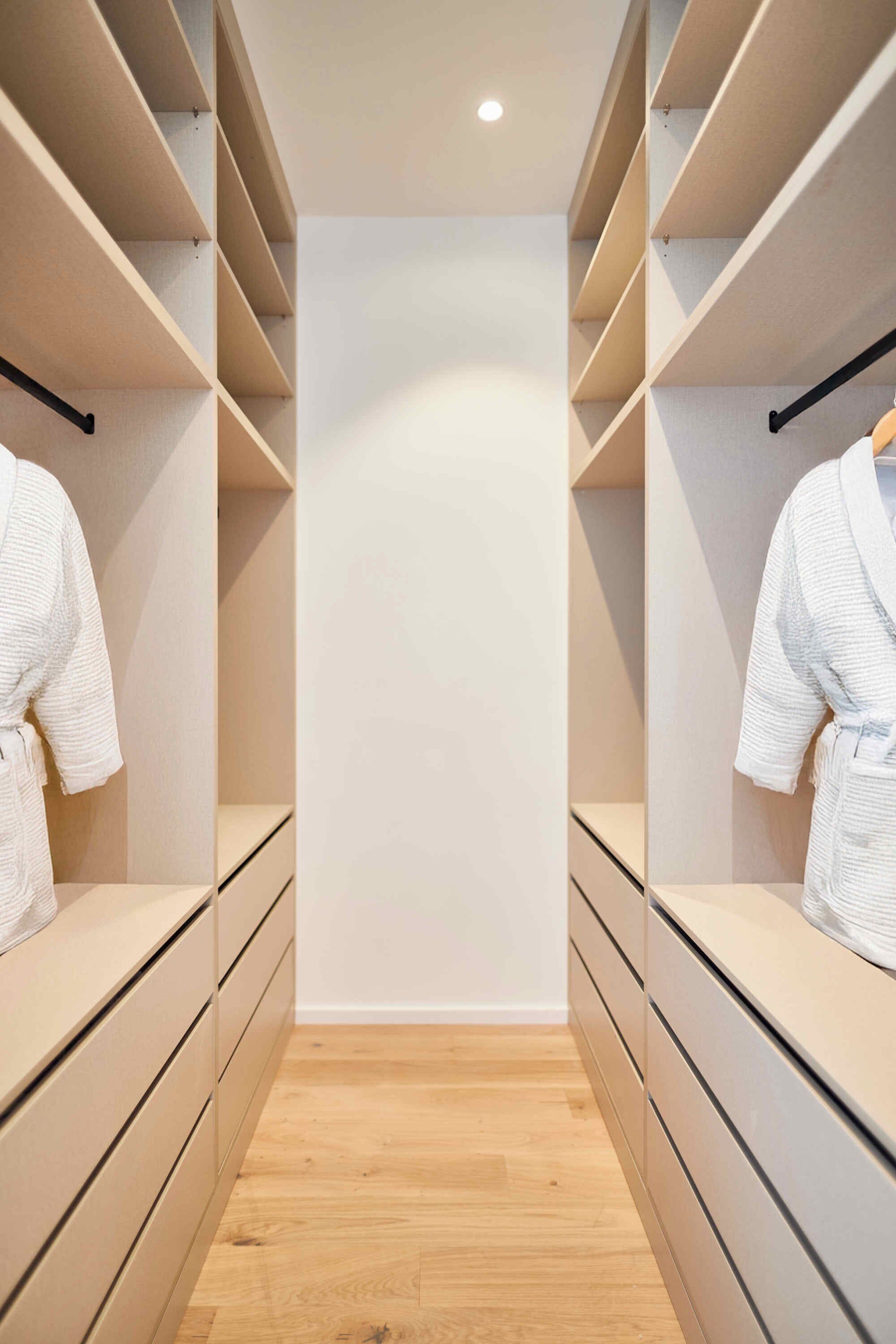 Un vestidor moderno con cajones y estantes de madera, que incluye dos colgadores para abrigos.