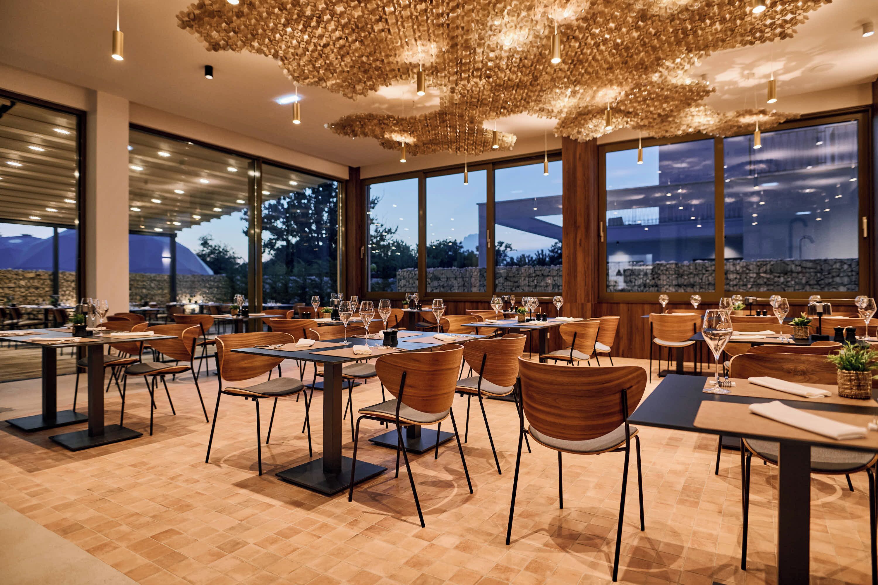 Un restaurante con varias mesas y sillas, ventanas amplias y un diseño de techo original.