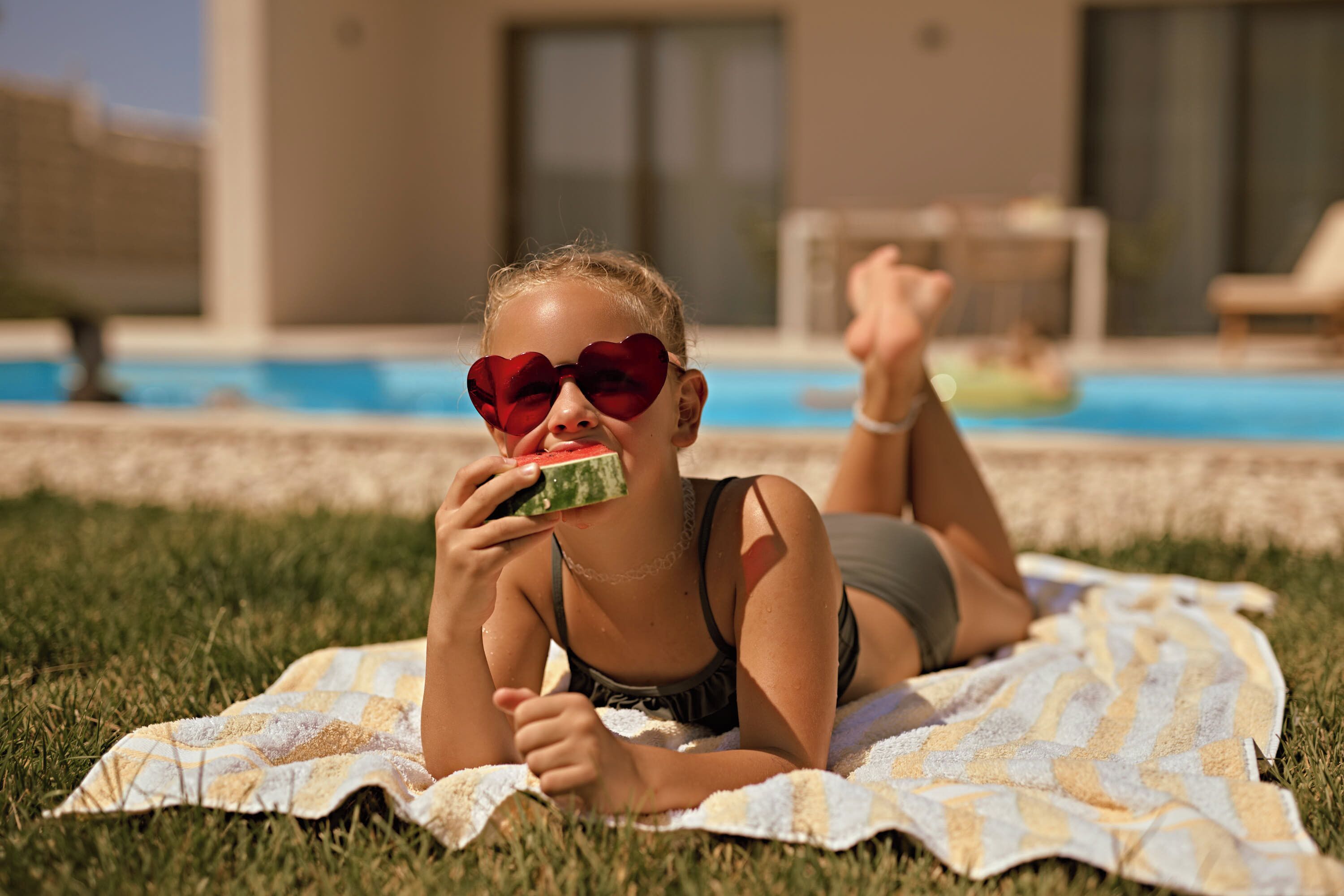 Una persona recostada sobre una toalla a cuadros junto a una piscina.