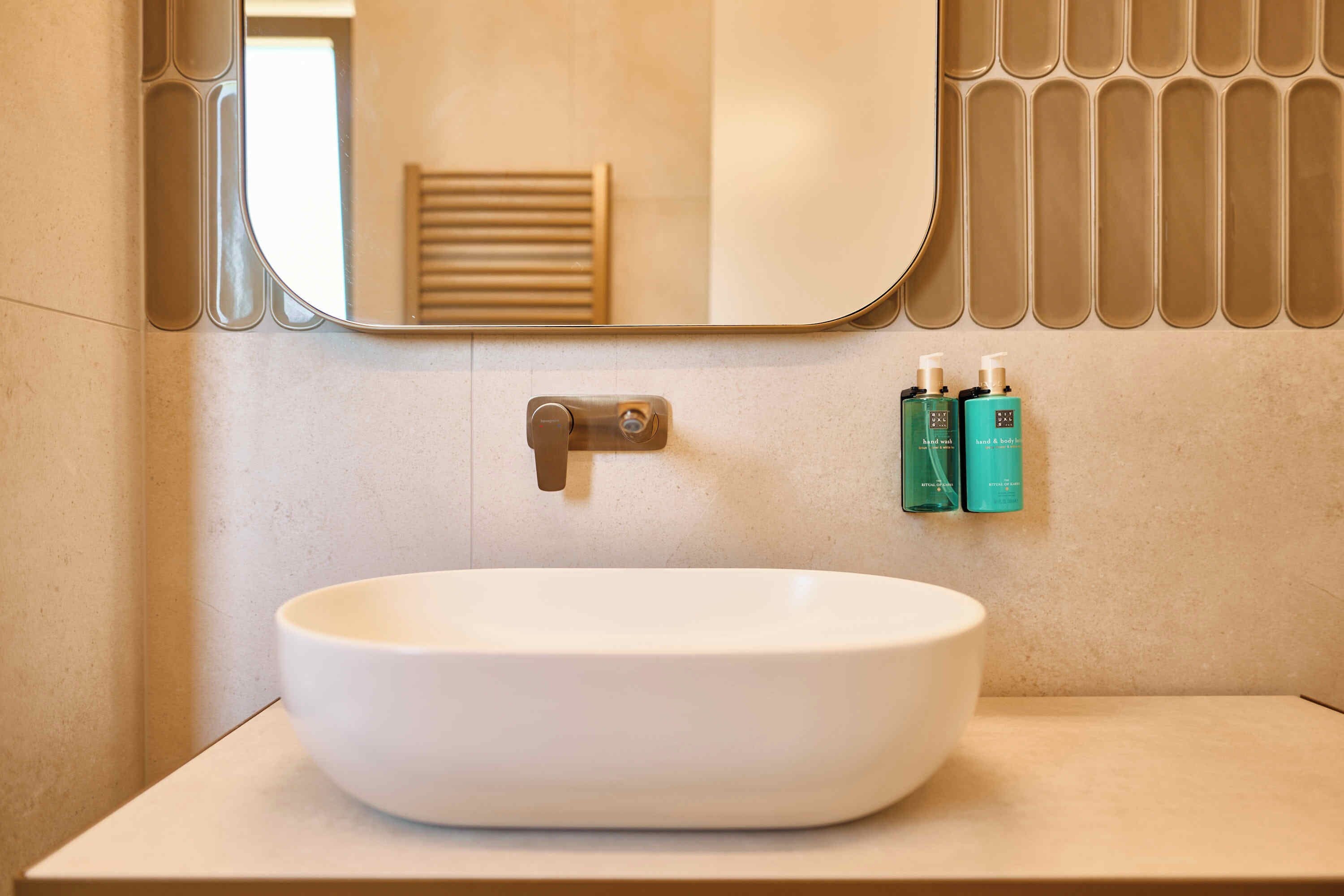 A bathroom with a white vessel sink, a mirror, and two toiletry bottles on the wall.