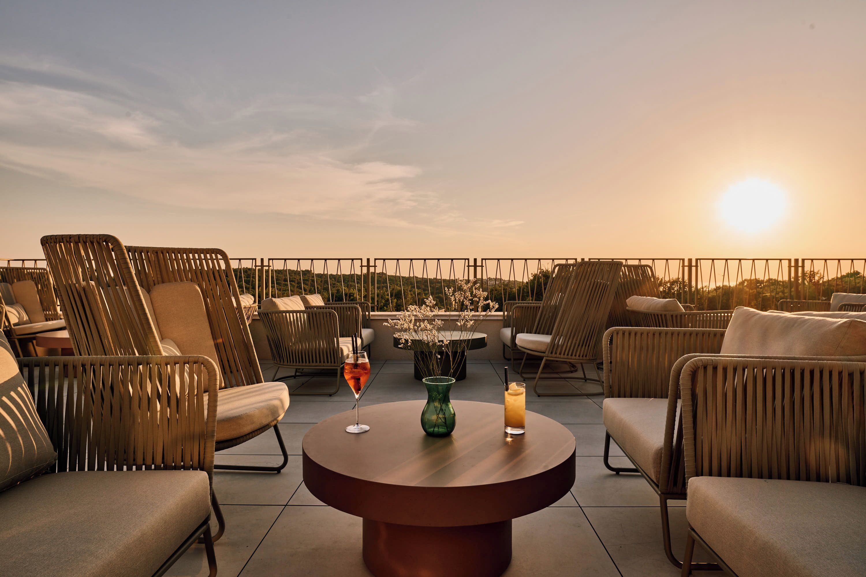 Een terras met rieten meubilair, een ronde tafel en uitzicht op de ondergaande zon.