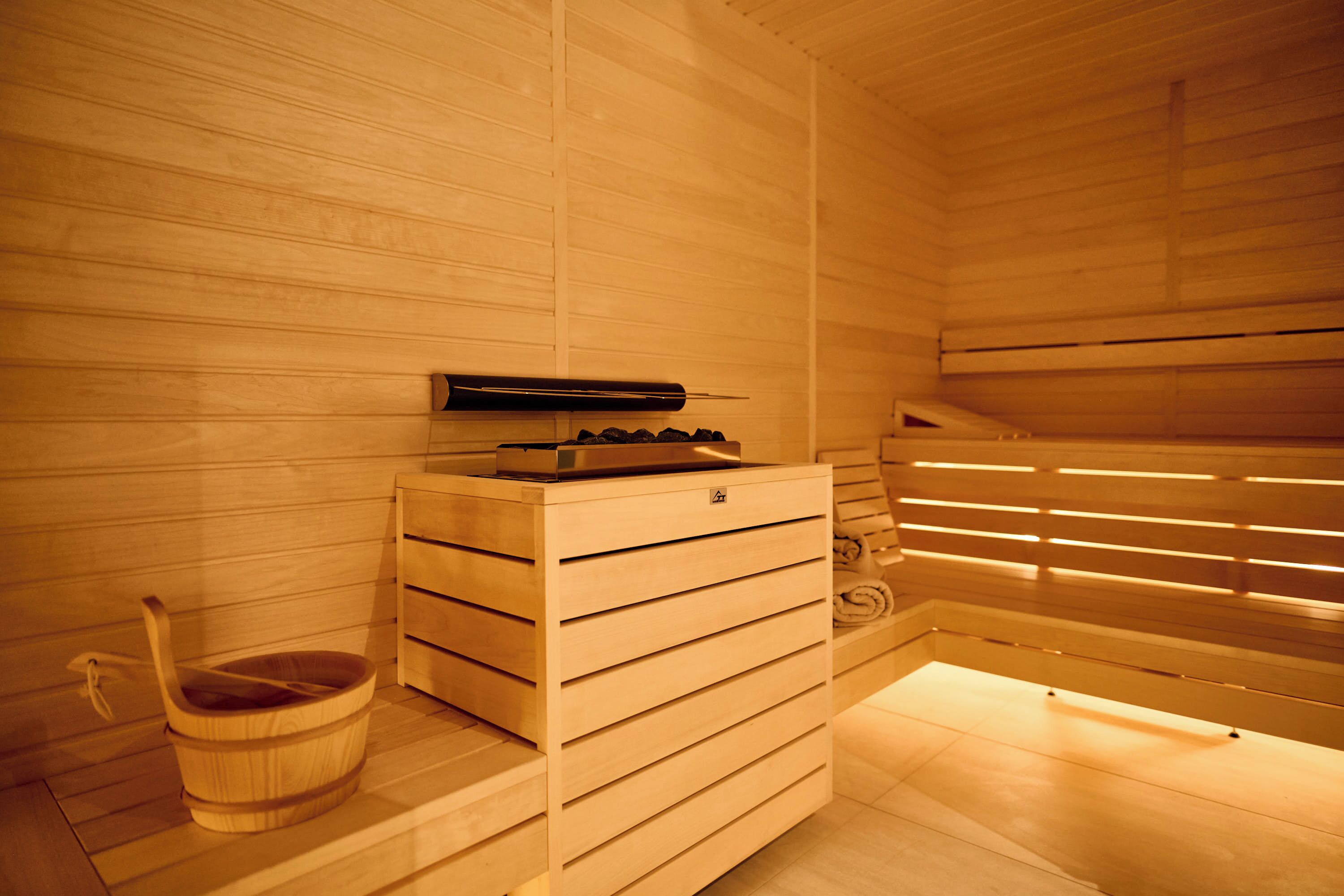 Un sauna avec des murs et des bancs en bois, un seau en bois et un appareil de chauffage pour sauna.
