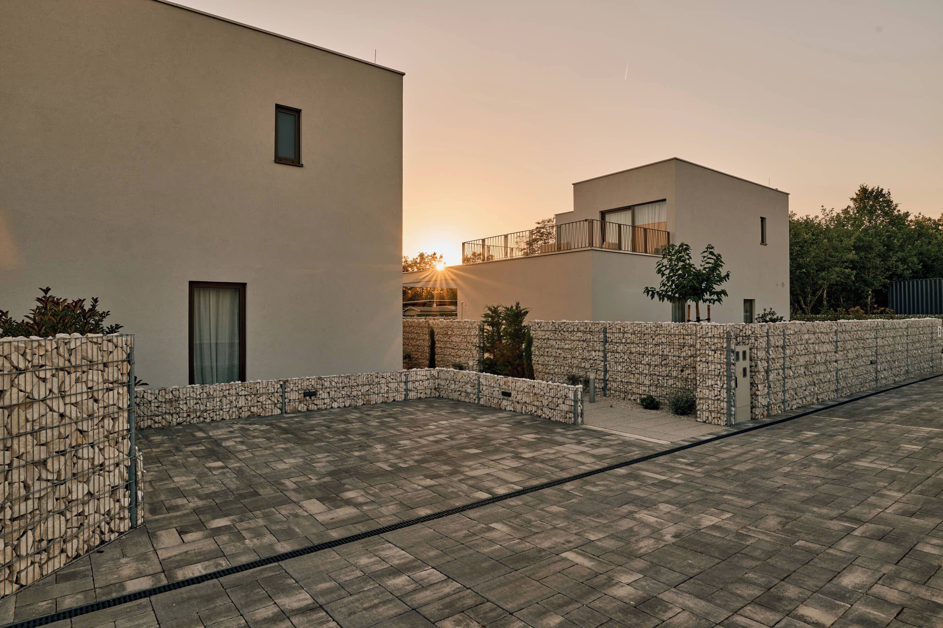 A modern building with a flat roof, a stone wall, and a paved courtyard.