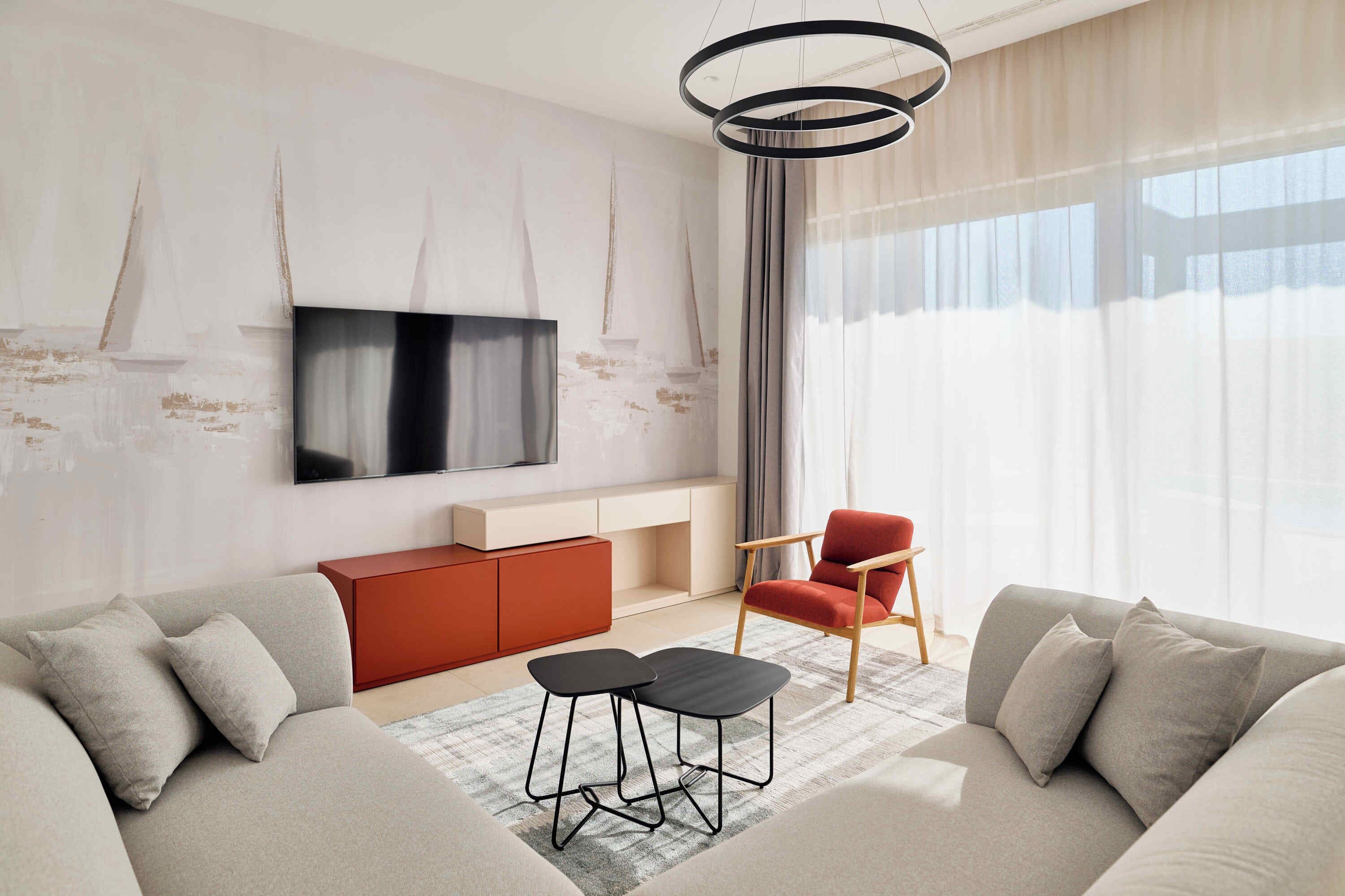 A modern living room with a sofa, a red chair, a black coffee table, and a TV mounted on the wall.