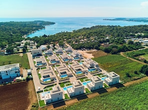 An aerial view of a modern resort with multiple buildings, swimming pools, and a coastal backdrop. - Taria Resort (Tar)