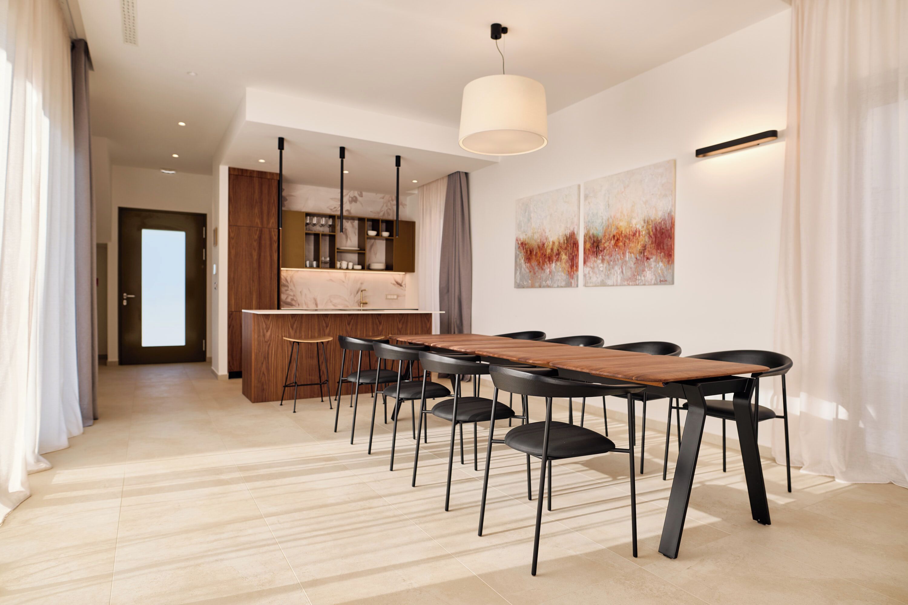 Un comedor moderno con una mesa de madera y sillas negras, una cocina al fondo y arte abstracto en la pared.