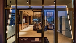 Un hall d’hôtel moderne avec un bar, des espaces pour s’asseoir et une vue à travers les portes vitrées.
