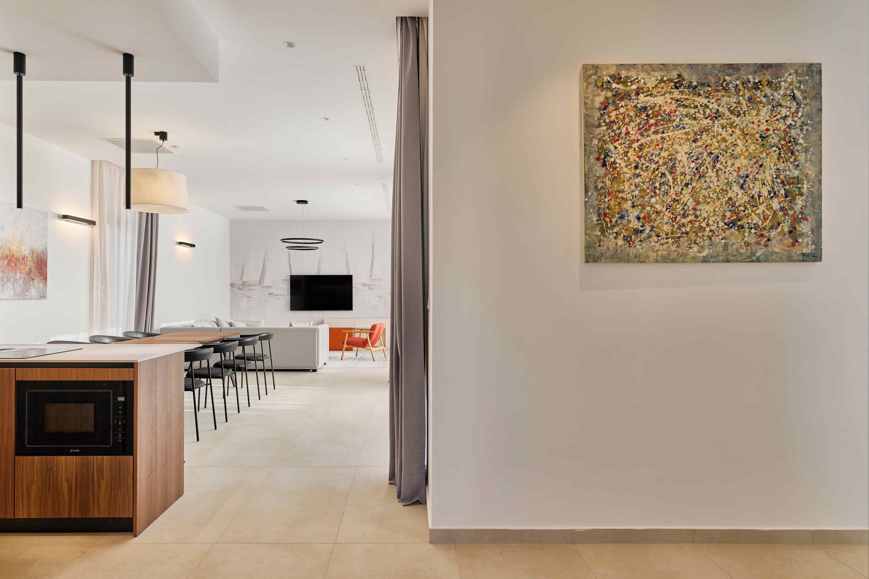 A modern kitchen with a built-in microwave, a dining area with chairs, and a large abstract painting on the wall.