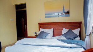 A hotel room with a large bed, a wooden headboard, and a painting of a lighthouse on the wall. - Plavender inn (Dar es Salaam)
