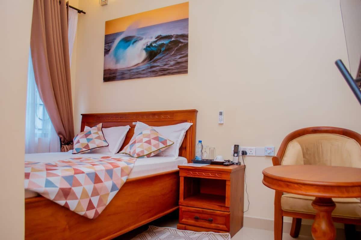Une chambre d’hôtel avec un lit, une table de chevet, une chaise et un tableau représentant une vague accroché au mur.