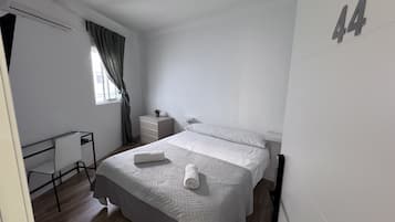 A bedroom with a bed, a desk, a dresser, and a window with curtains.