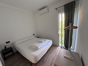 A single bed with white linens, a bedside table with a lamp, a remote control, and a window with curtains. - MÜDE Hostel (Torremolinos)