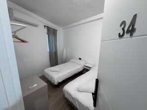 A hotel room with two beds, a bedside table, a hanging coat rack, and a number '34' on the wall. - MÜDE Hostel (Torremolinos)