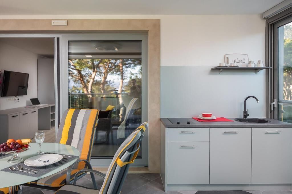 Una cocina moderna con puerta de cristal que da a un balcón, una zona de comedor con una silla a rayas y un televisor montado.