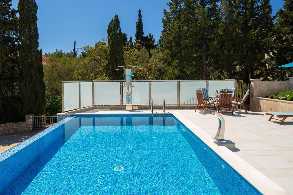 A rectangular swimming pool with clear blue water, surrounded by a tiled deck and a glass fence.