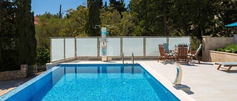 Une piscine rectangulaire à l’eau d’un bleu cristallin, entourée d’une terrasse carrelée et d’une clôture en verre.