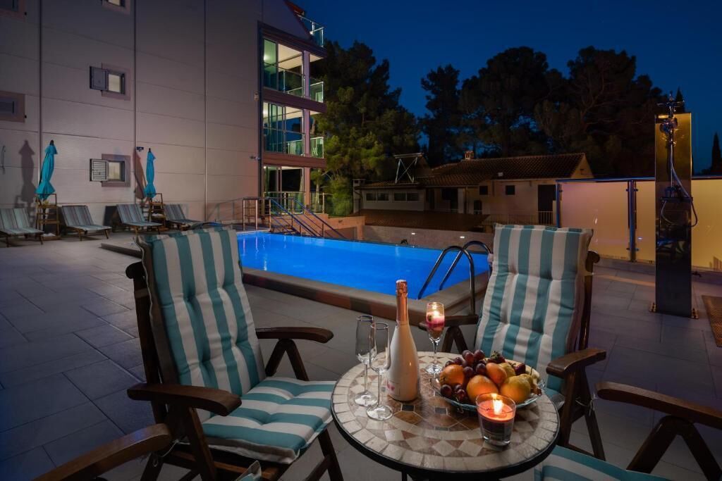 A poolside area with lounge chairs, a table with a bottle and fruit, and a building in the background.