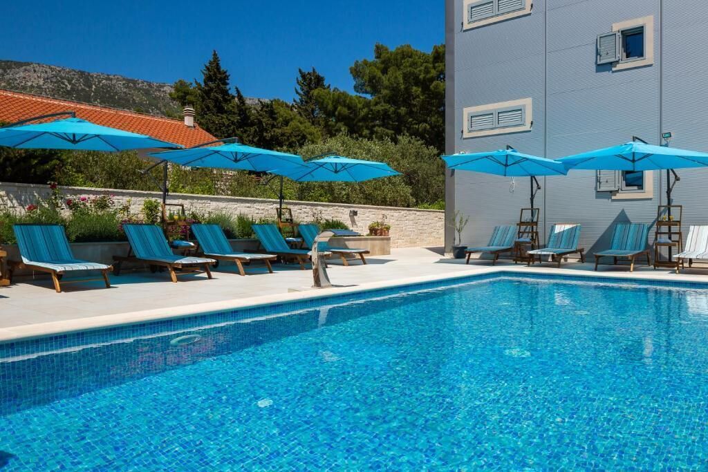 Une piscine à l’eau légèrement bleutée, entourée de chaises longues et de parasols bleus.