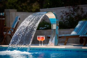 En pool med et vandfald, to liggestole og et glas med drik.
