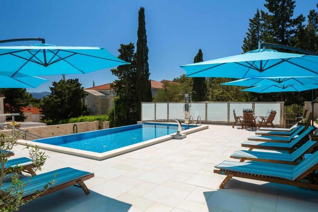 Piscina com espreguiçadeiras e guarda-sóis, ladeada por um deck ladrilhado e vegetação.