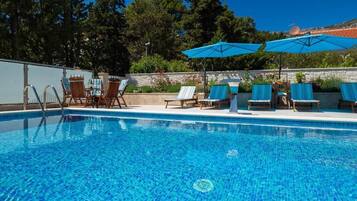 A swimming pool with lounge chairs and umbrellas, surrounded by a stone wall and trees.