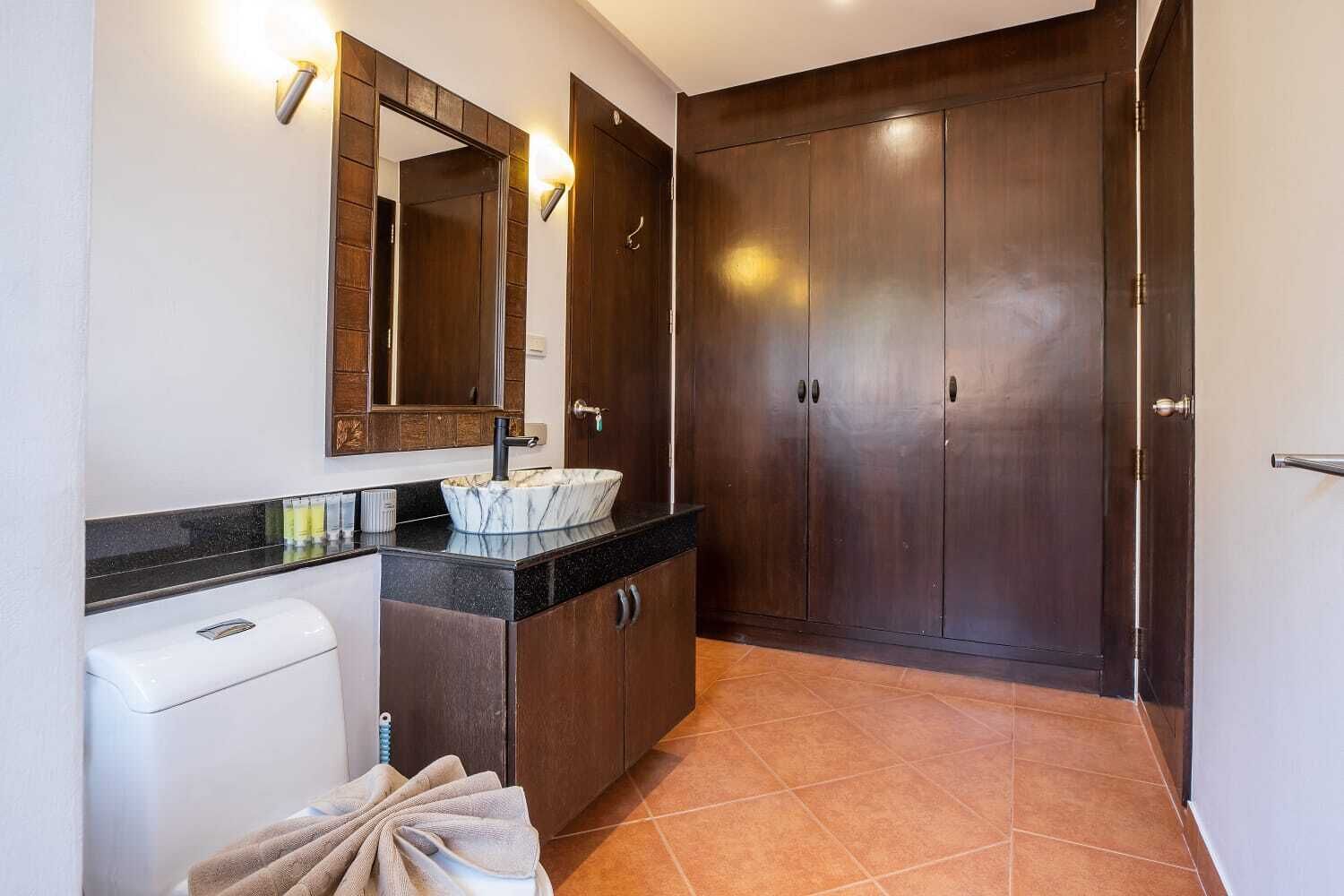 A bathroom with a marble sink, dark wooden cabinets, a toilet, and a towel rack.