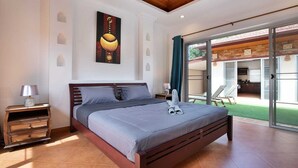 A bedroom with a wooden bed, a nightstand, a painting, and a sliding glass door to a patio. - Balinese 3BR Pool Villa Freya in Rawai (Rawai)