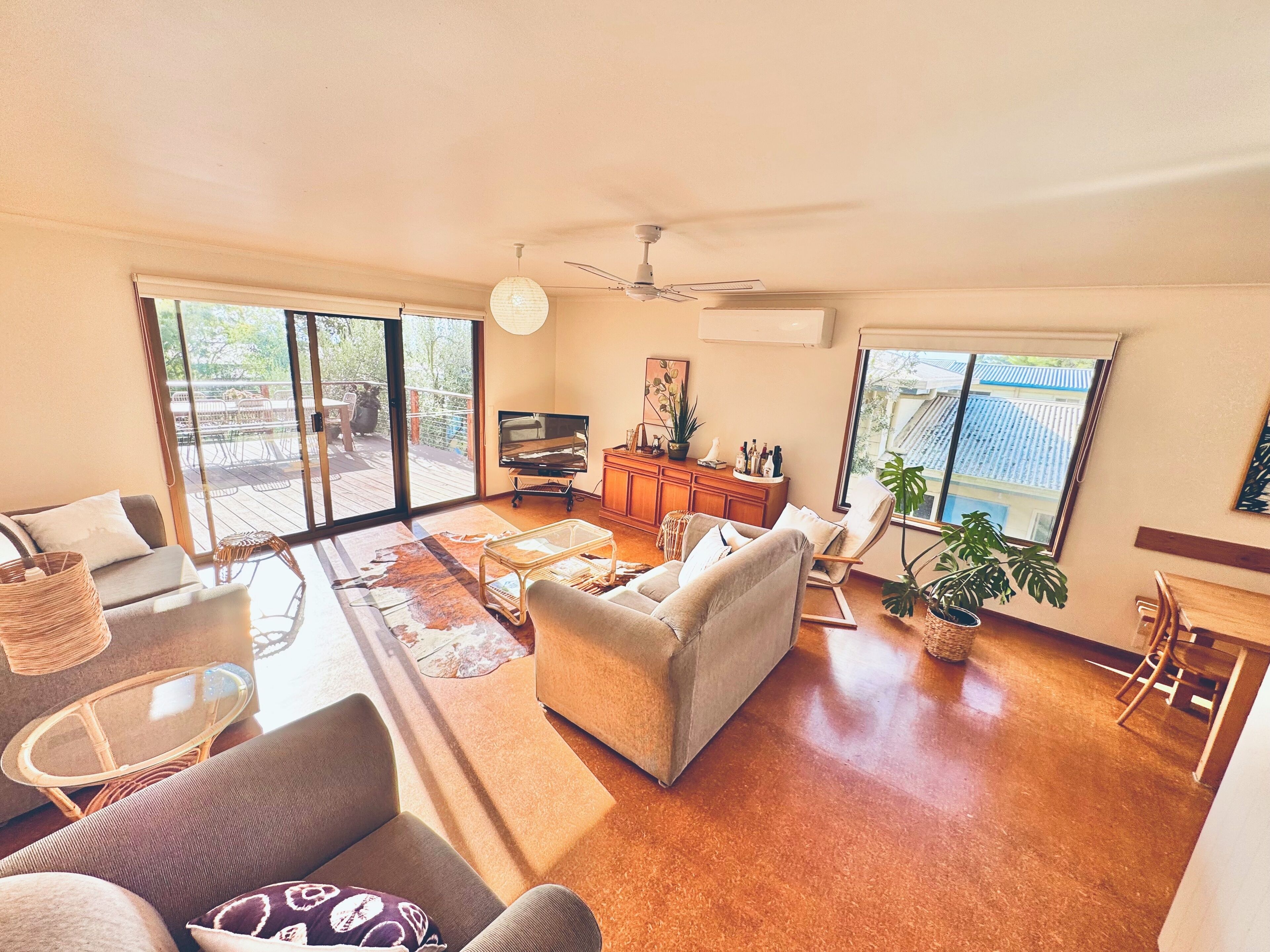 A spacious living room with a sofa, chairs, a TV, and a ceiling fan.