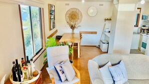 Un salon confortable avec un canapé, une table à manger et une chaise. Une fenêtre offre une vue sur la verdure environnante.