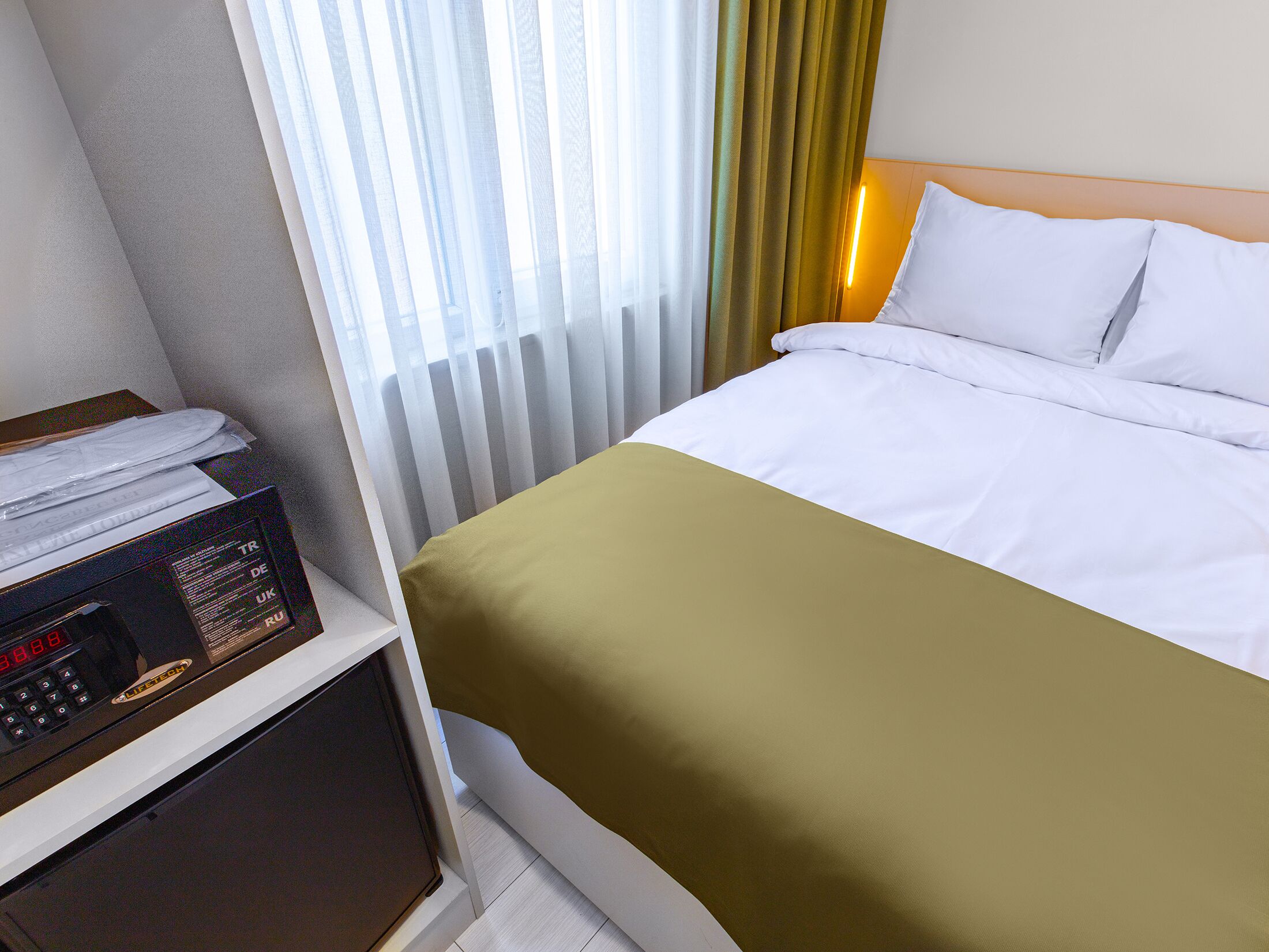 Quarto de hotel com cama, escrivaninha com computador e janela com cortinas.