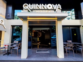 The entrance to the Quinnova Hotel with a modern design, featuring a prominent sign and outdoor seating area.